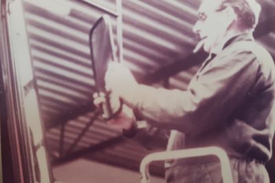 Jos Geudens met sigaret in de mond aan het sleutelen in eigen garage te Arendonk circa 1980